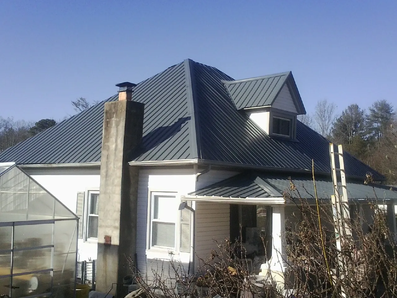 Dark blue standing seam metal roof on a white farmhouse with dormer — Slate & Tile Roof Repair by Roofing Brothers in Midvale