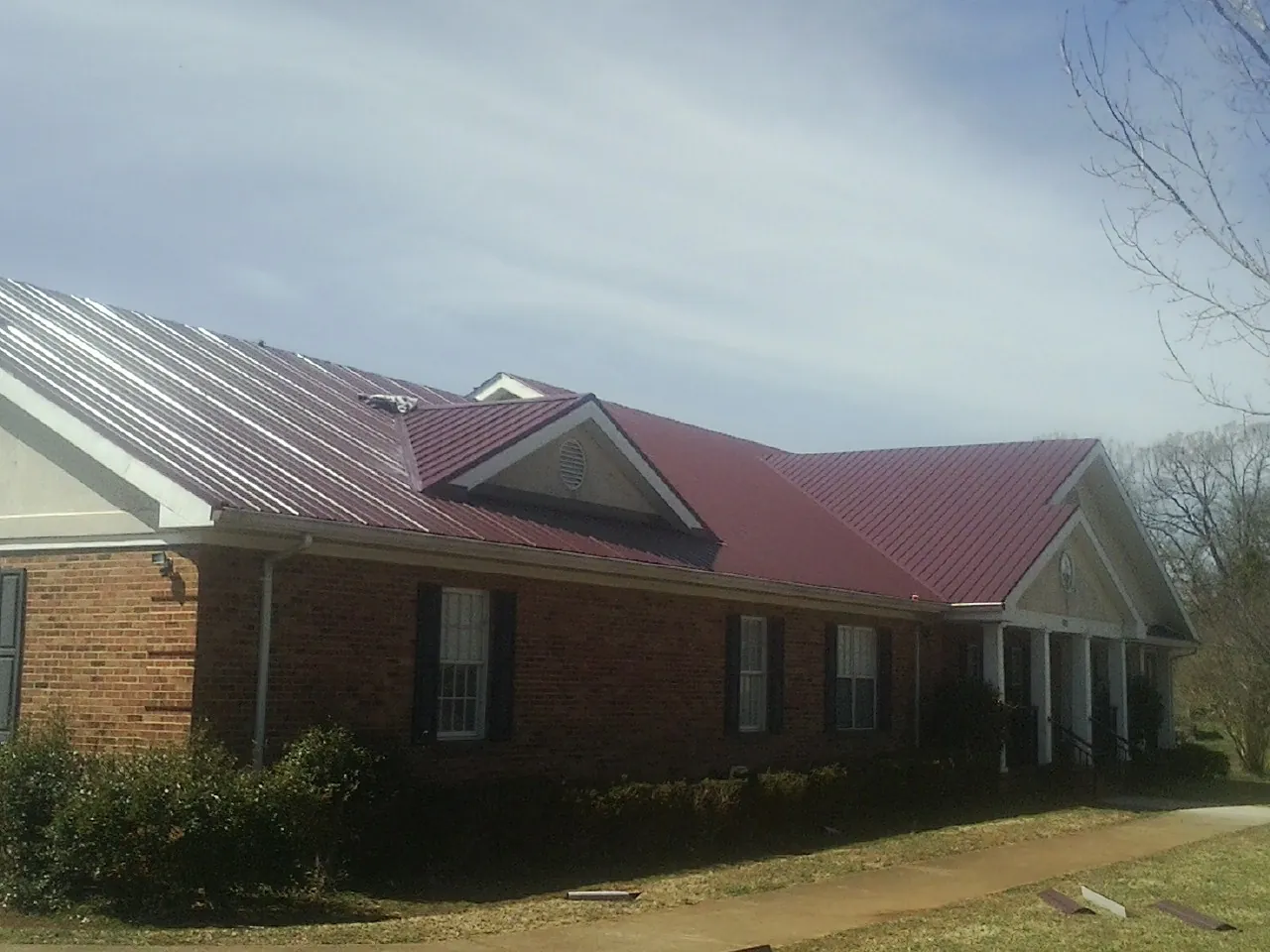 Red metal roof with gabled entries on a long brick building, from a Hail Damage Roof Repair job in Midvale