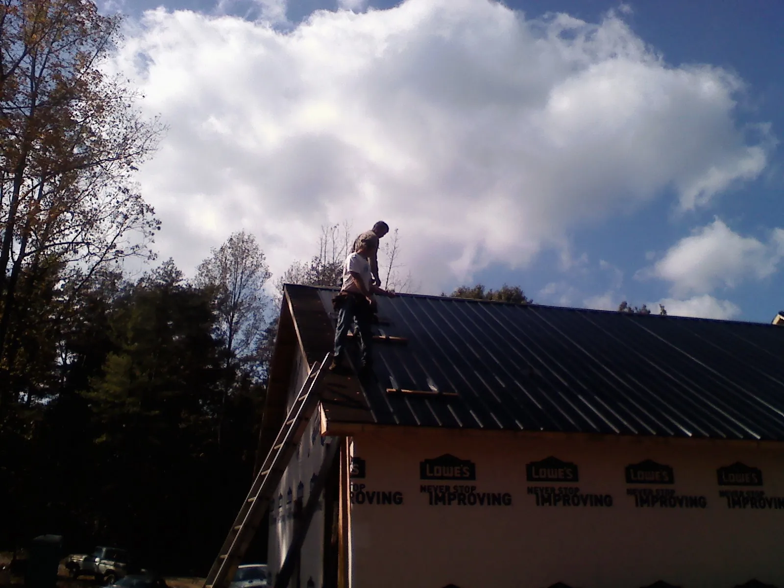 Roofer fastening dark metal panels high against a cloudy sky, from a Roof Inspection job in Midvale