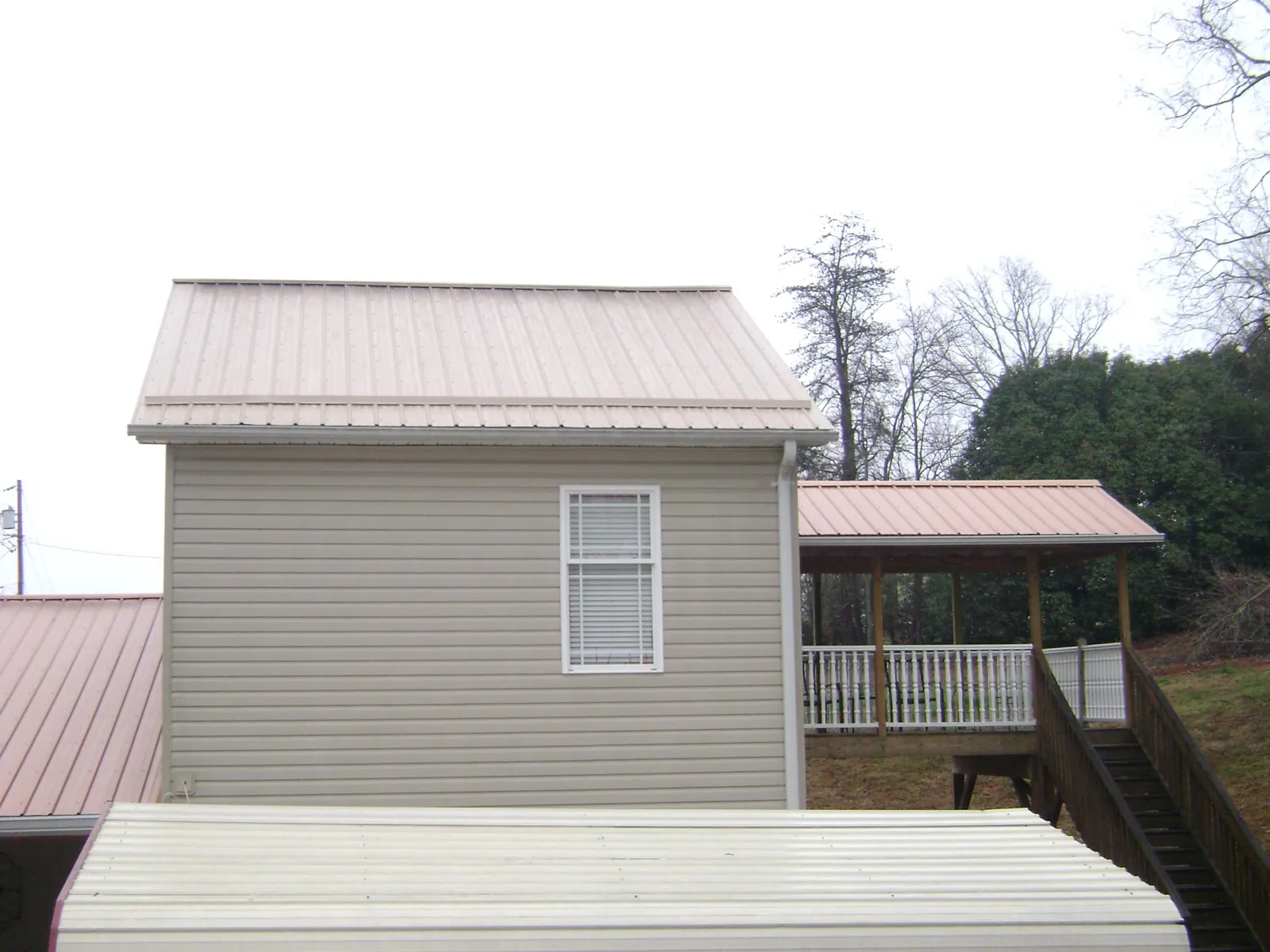 Tan metal roofs on a two story addition and attached porch, from a Roof Replacement job in Midvale